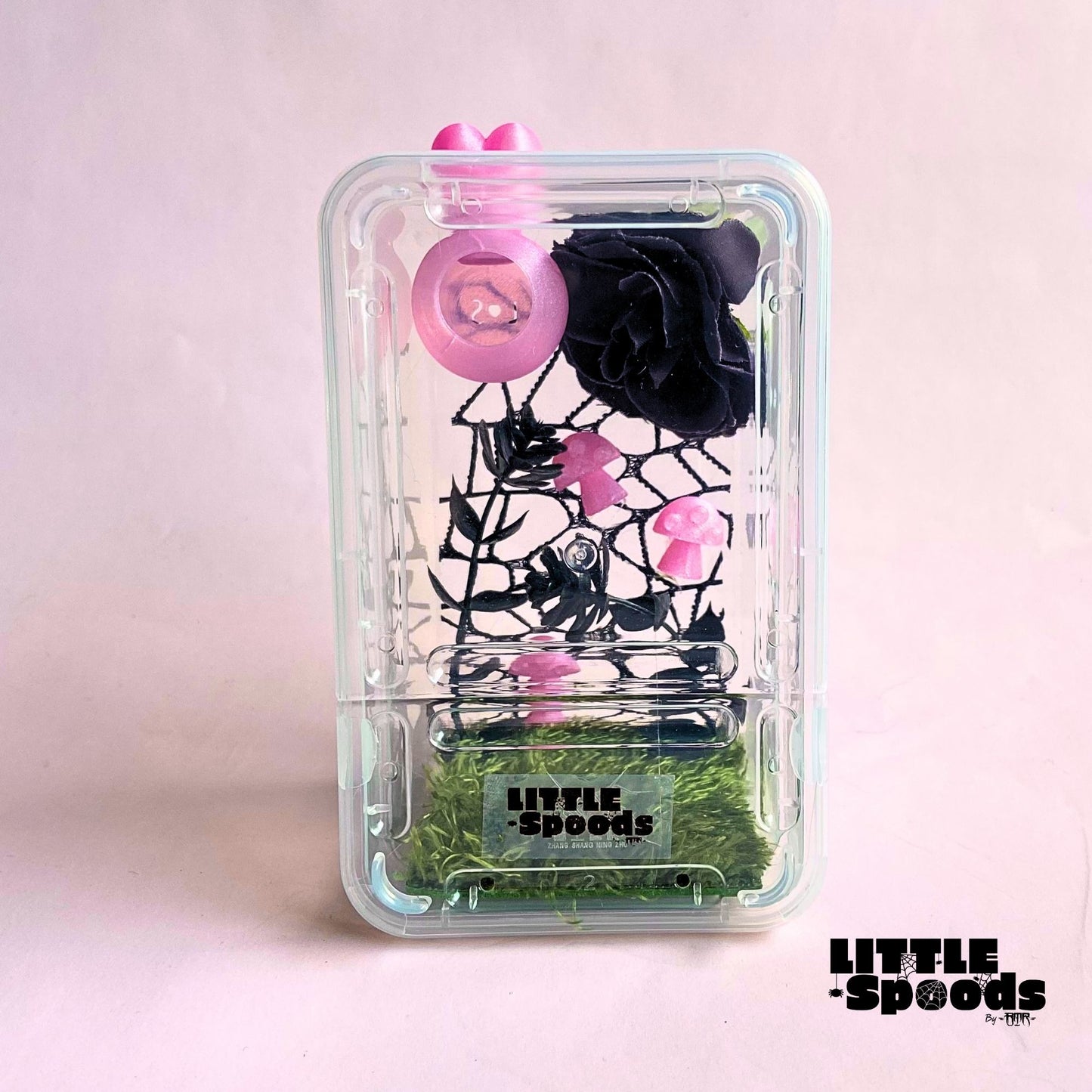 Pink decorated juvenile jumping spider enclosure with magnetic hide, black flower, mushrooms, and spider-safe décor.
